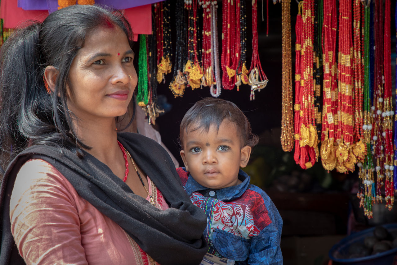 A woman holds small child in front of necklaces