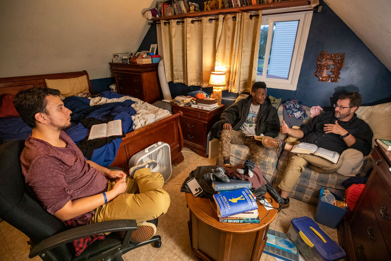 older man talks with two younger men in the living room