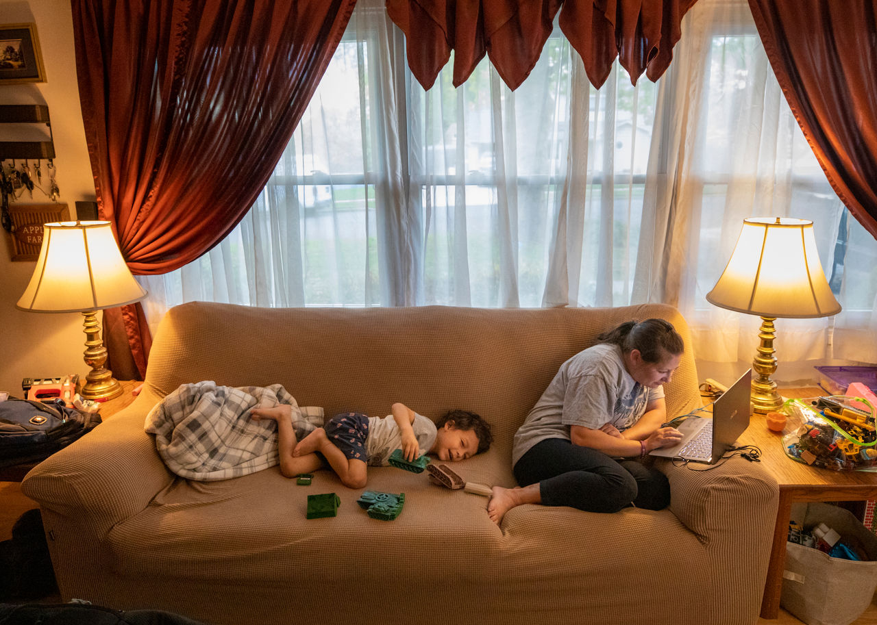 little boy plays on couch next to his mom as she works on her laptop