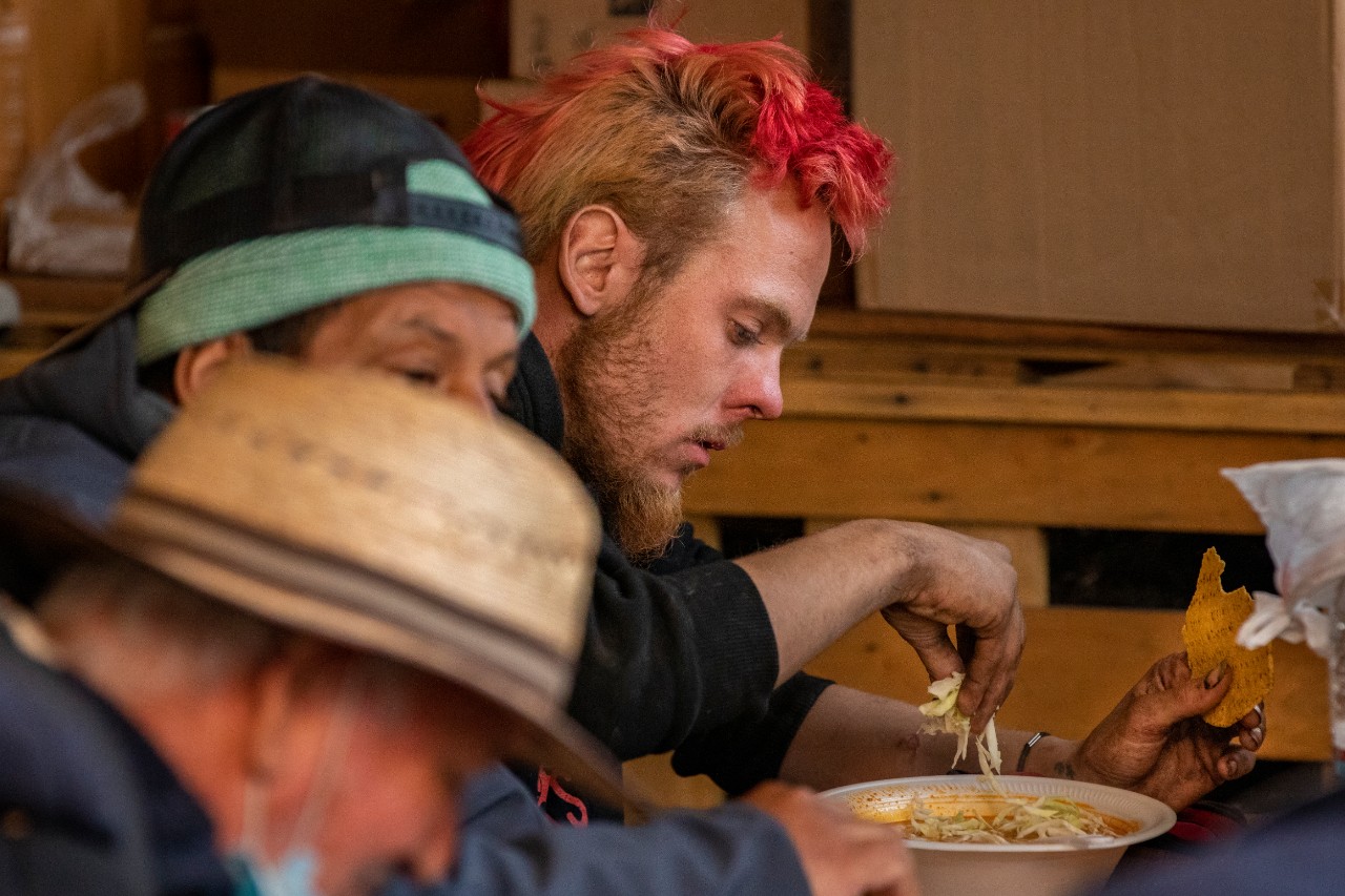 Homeless men from a nearby street mission eat a free lunch of hominy soup with shredded cabbage and tortillas during the Boxes of Love® distribution at Agape Church.