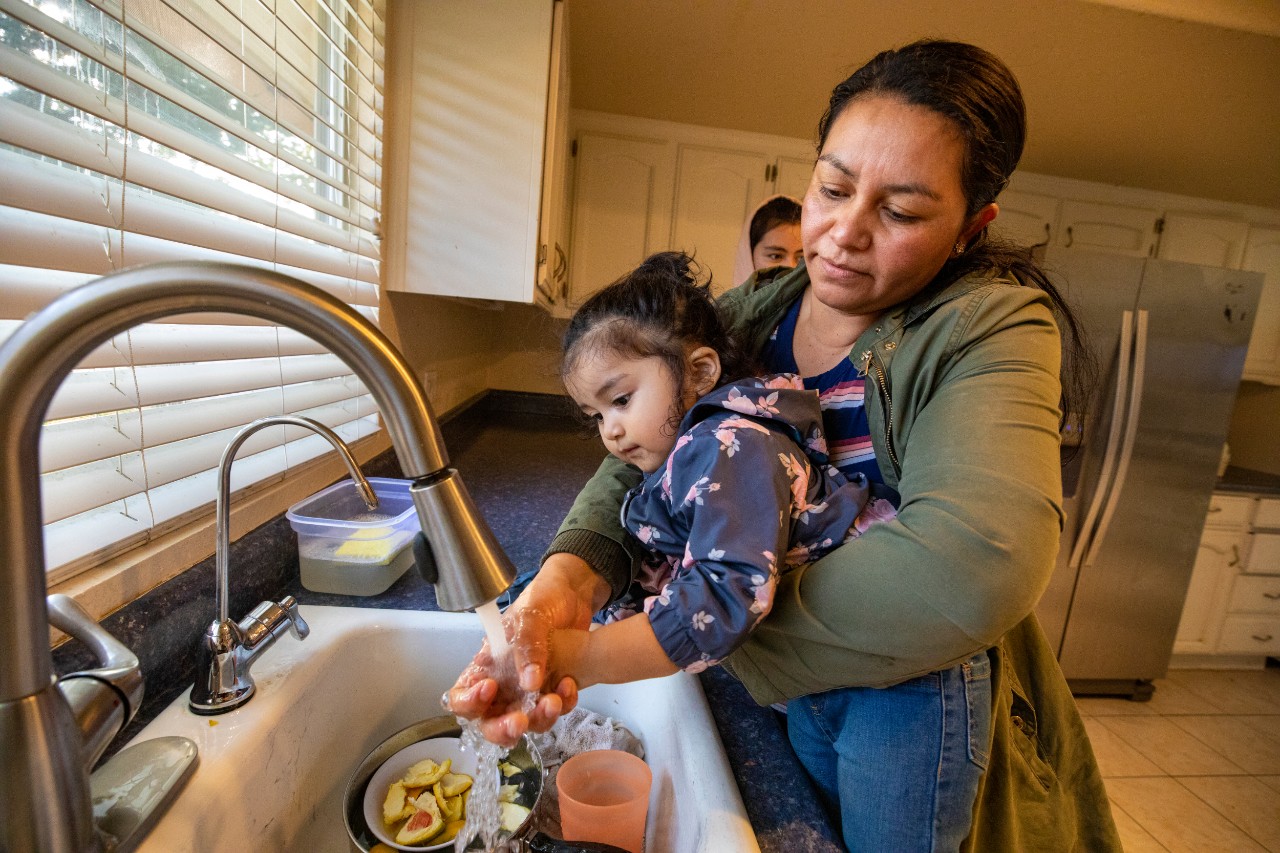 In Maria’s kitchen, Rossana helps Emma wash her hands after playing outside.