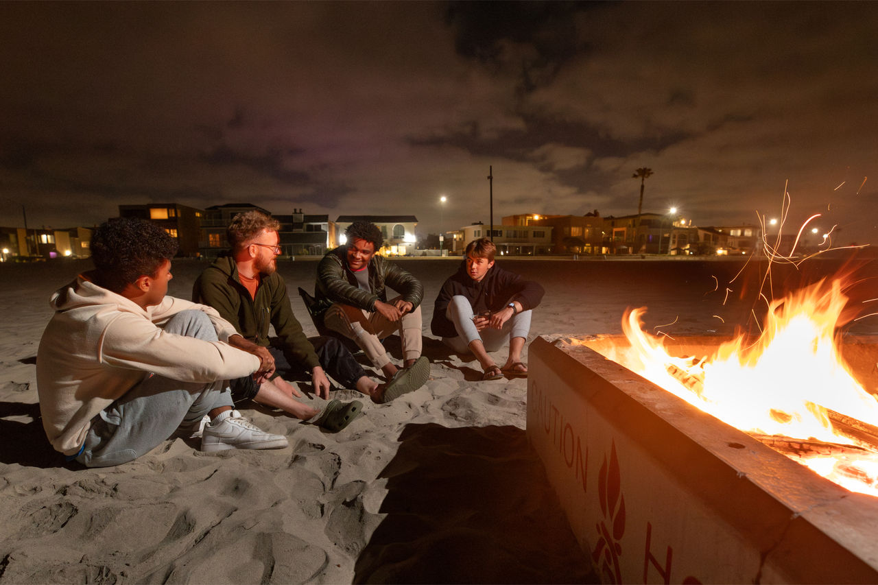 Adam, Tater, and Logan sit around a beachside fire with their discipleship group leader, James Ward (second from left)