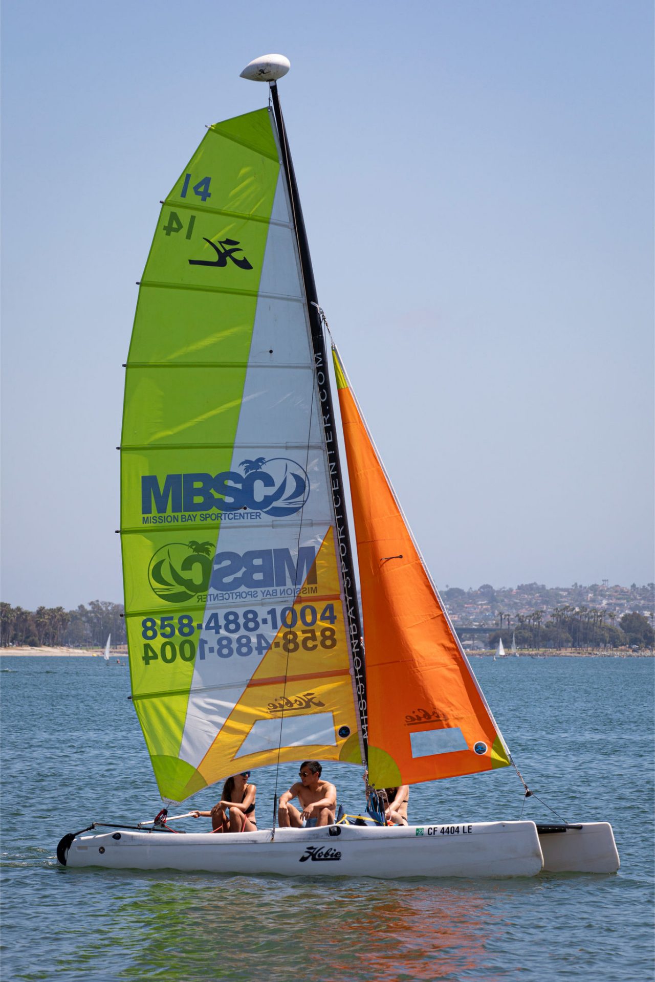 a catamaran with green and orange sail with three sailors