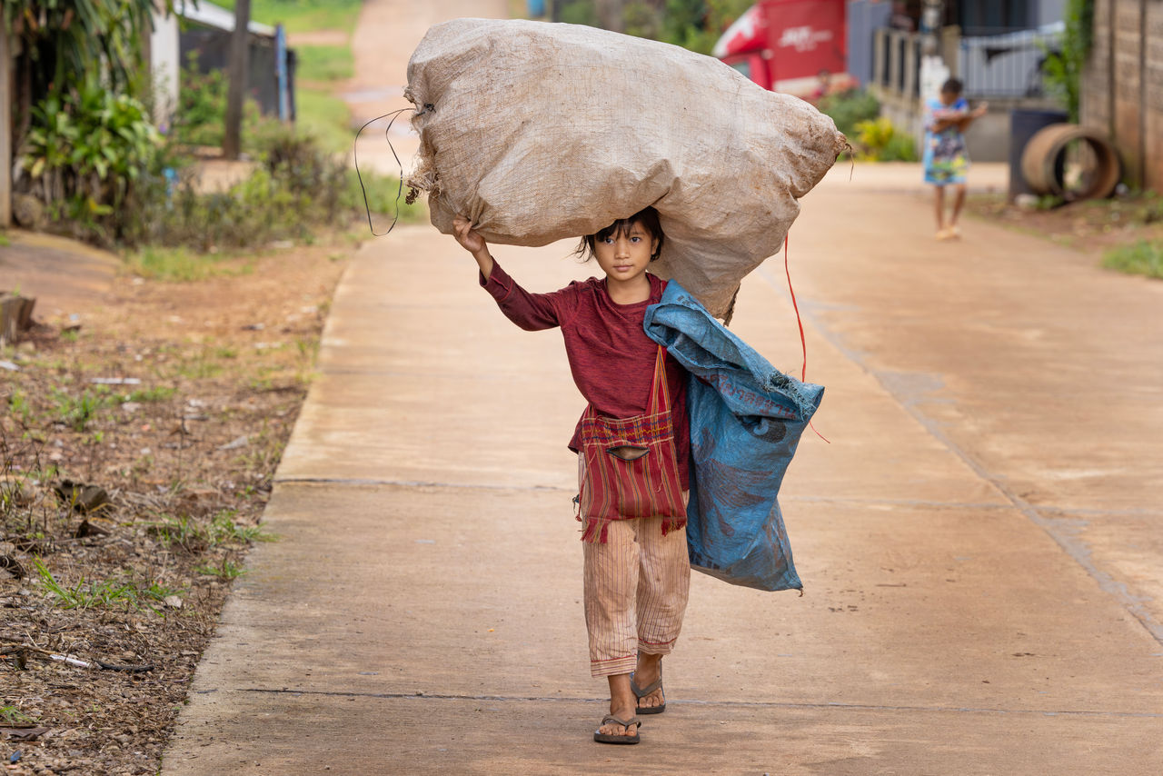 child carrying sack on head walking on a road